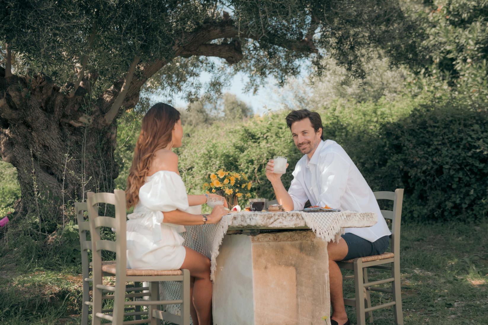 Guests enjoying a meal under the centuries-old olive tree, during their couples holiday in Greece at Kinsterna Hotel, Monemvasia.